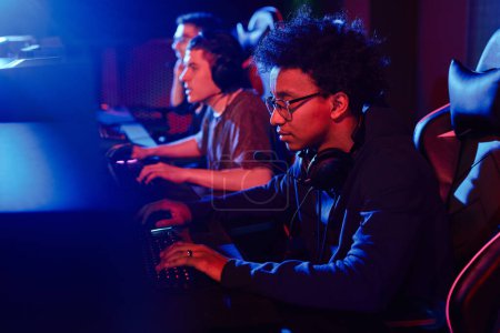 Photo for Side view portrait of young African American man playing video games with cyber sports team in neon light - Royalty Free Image