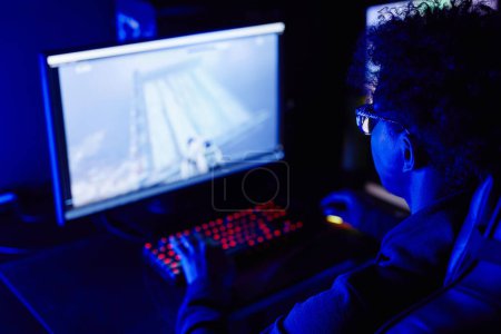 Foto de Vista sobre el hombro del joven negro jugando videojuegos en el club de ciberdeportes con iluminación de neón azul - Imagen libre de derechos