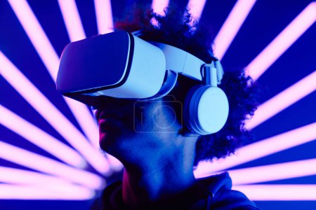 Téléchargez les photos : Portrait futuriste en gros plan de jeune homme portant un casque VR avec des faisceaux lumineux au néon, espace de copie - en image libre de droit