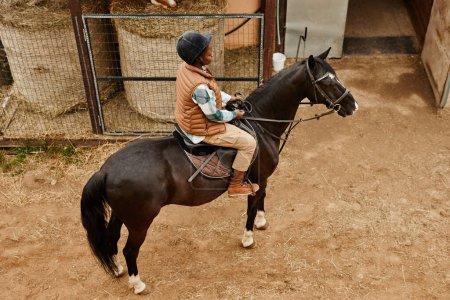 Téléchargez les photos : Portrait en grand angle d'une jeune femme chevauchant un cheval dans un ranch et menant à des écuries, espace de copie - en image libre de droit