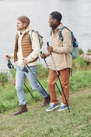 Téléchargez les photos : Deux jeunes hommes utilisant des bâtons pendant la marche nordique dans le parc à l'extérieur - en image libre de droit