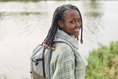 Téléchargez les photos : Portrait de jeune fille africaine avec une coiffure élégante souriant à la caméra tout en marchant à l'extérieur - en image libre de droit