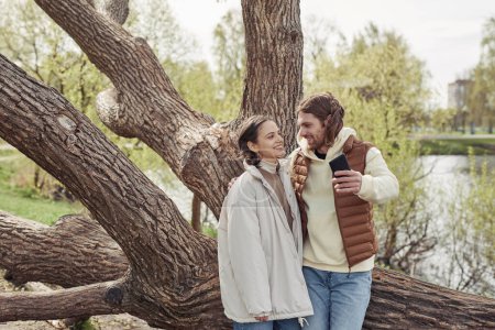 Téléchargez les photos : Jeune couple heureux profiter de l'autre lors de leur promenade dans le parc, ils font selfie contre grand arbre - en image libre de droit
