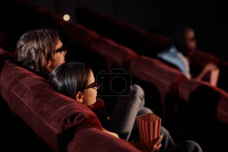 Vue arrière du jeune couple regardant un film 3d en lunettes sur des fauteuils confortables au cinéma