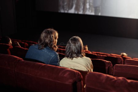 Téléchargez les photos : Vue arrière de jeunes couples assis sur des fauteuils confortables regardant un film ensemble pendant leur rendez-vous au cinéma - en image libre de droit