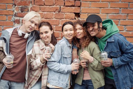 Téléchargez les photos : Plusieurs adolescents interculturels heureux avec des lunettes de soude debout près de l'autre contre le mur de briques et en regardant la caméra - en image libre de droit