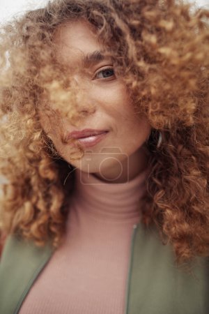 Photo for Young stylish woman in beige turtleneck and casual jacket with her long and thick wavy hair covering part of face looking at camera - Royalty Free Image