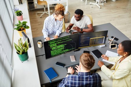 Téléchargez les photos : Vue en grand angle des programmeurs assis à table avec moniteurs d'ordinateur et écriture de codes en équipe au bureau - en image libre de droit