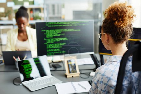 Foto de Vista trasera de una joven programadora sentada en su lugar de trabajo frente a monitores y trabajando con códigos de programa - Imagen libre de derechos