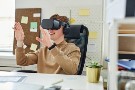 Photo for Young programmer sitting at table at office and gesturing, he testing virtual reality glasses - Royalty Free Image