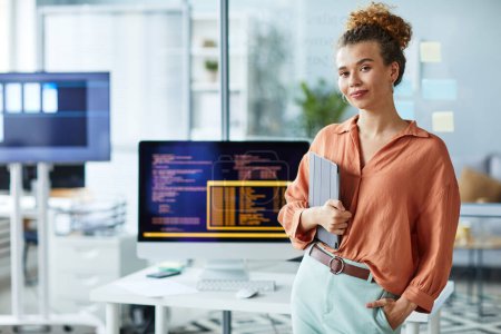 Porträt einer jungen Programmiererin mit digitalem Tablet, die an ihrem Arbeitsplatz mit dem Computer in die Kamera blickt