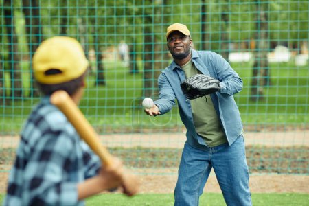 Téléchargez les photos : Un homme africain attrape une balle avec un gant lancé par son fils pendant un match de baseball en plein air - en image libre de droit