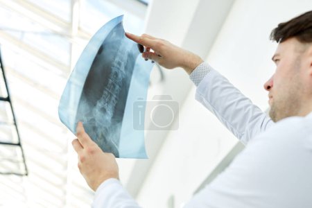 Photo for Low angle view of expert doctor holding x ray image and examining spine injury, copy space - Royalty Free Image