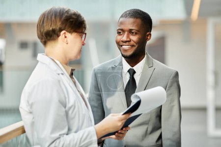 Foto de Retrato en la cintura de un hombre de negocios afroamericano sonriente hablando con una colega en el edificio de oficinas - Imagen libre de derechos