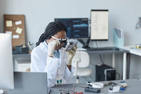Foto de Retrato de una joven mujer negra que usa visera de aumento e inspecciona la pieza de hardware en el laboratorio de ingeniería - Imagen libre de derechos
