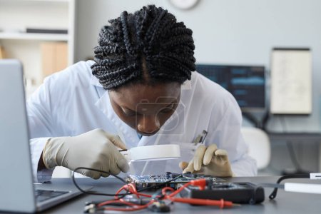 Téléchargez les photos : Gros plan de la jeune scientifique inspectant le matériel avec loupe dans un laboratoire d'ingénierie - en image libre de droit