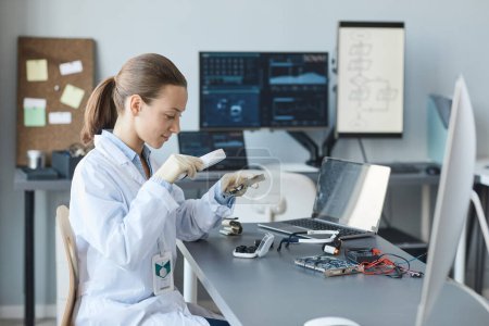 Foto de Retrato de vista lateral de una joven científica inspeccionando hardware con lupa en laboratorio de ingeniería, espacio de copia - Imagen libre de derechos