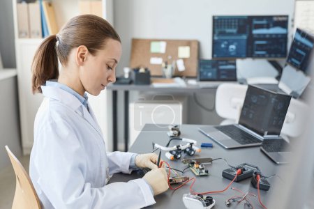 Photo for Side view portrait of female lab technician checking hardware parts at quality control station, copy space - Royalty Free Image