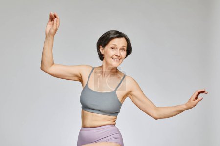 Photo for Minimal waist up portrait of carefree mature woman wearing neutral underwear dancing against grey background, body positivity concept, copy space - Royalty Free Image