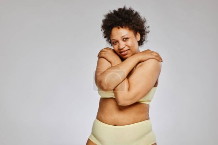 Photo for Minimal waist up portrait of adult black woman wearing underwear and covering body while standing against grey background - Royalty Free Image