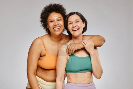 Foto de Cintura mínima hacia arriba retrato de dos mujeres reales que usan ropa interior y se ríen felizmente contra el fondo gris - Imagen libre de derechos
