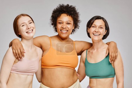 Téléchargez les photos : Taille minimale vers le haut groupe diversifié de vraies femmes portant des sous-vêtements et riant joyeusement sur fond gris - en image libre de droit