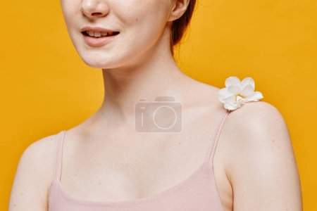 Téléchargez les photos : Gros plan minimal de la jeune femme délicate avec des fleurs sur une peau claire sur fond jaune vif - en image libre de droit