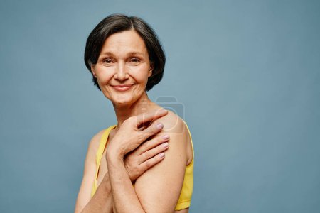 Photo for Candid portrait of mature woman smiling at camera while posing elegantly against pastel blue background, copy space - Royalty Free Image