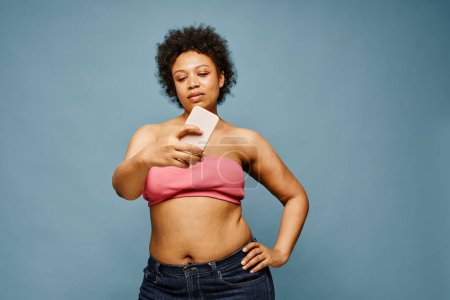 Foto de Retrato de la cintura hacia arriba de la mujer negra confiada tomando la foto del selfie contra fondo azul pastel, espacio de la copia - Imagen libre de derechos