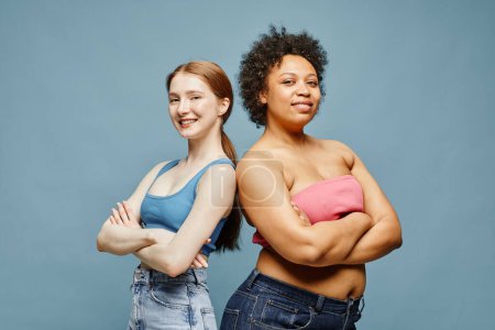 Foto de Candid cintura hacia arriba retrato de dos mujeres jóvenes seguras de pie sobre fondo azul pastel y sonriendo - Imagen libre de derechos