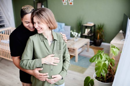 Photo for High angle portrait of happy lesbian couple expecting baby and embracing lovingly with hands on pregnant belly, copy space - Royalty Free Image