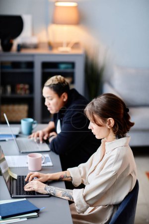 Téléchargez les photos : Portrait vertical latéral de deux femmes utilisant des ordinateurs au travail à la maison ensemble - en image libre de droit