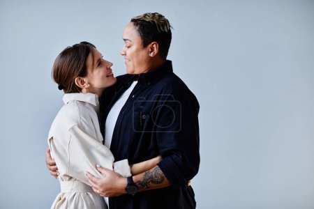 Foto de Mínima vista lateral retrato de feliz pareja gay abrazando contra fondo azul, espacio de copia - Imagen libre de derechos