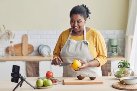 Photo for Portrait of young black woman cooking healthy meal in kitchen and recording video, copy space - Royalty Free Image