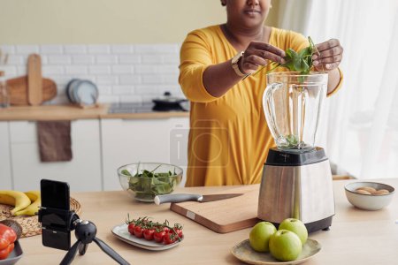 Photo for Cropped shot of black woman putting spinach in blender while making healthy smoothie at home, copy space - Royalty Free Image