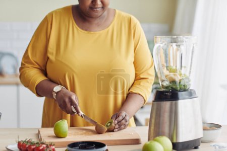 Foto de Primer plano de la mujer negra cortando frutas mientras hace comida saludable en la cocina y filmando video de cocina, espacio para copiar - Imagen libre de derechos