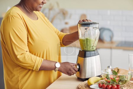 Téléchargez les photos : Vue latérale gros plan de la femme noire en utilisant un mélangeur tout en faisant un smoothie sain à la maison cuisine, copier l'espace - en image libre de droit