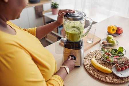 Téléchargez les photos : Gros plan angle de femme noire en surpoids utilisant un mélangeur tout en faisant un smoothie sain à la maison cuisine - en image libre de droit