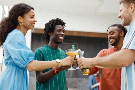 Téléchargez les photos : Divers groupes de jeunes dégustant des boissons à la fête en terrasse extérieure et trinquant avec des lunettes - en image libre de droit