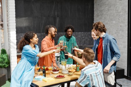Photo for Diverse group of friends enjoying dinner party at outdoor terrace in sunlight and clinking glasses in celebration - Royalty Free Image