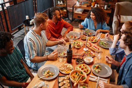 Téléchargez les photos : Vue en angle élevé à divers groupes de jeunes profitant d'un dîner à table dans un cadre confortable - en image libre de droit