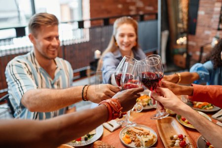 Photo for Closeup of young people toasting with wine glasses while celebrating dinner party together, copy space - Royalty Free Image