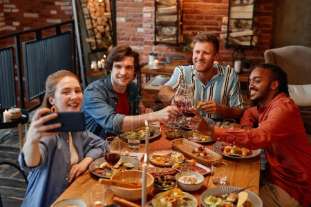 Photo for High angle view at group of friends taking selfie photo at table during dinner party and clinking glasses - Royalty Free Image