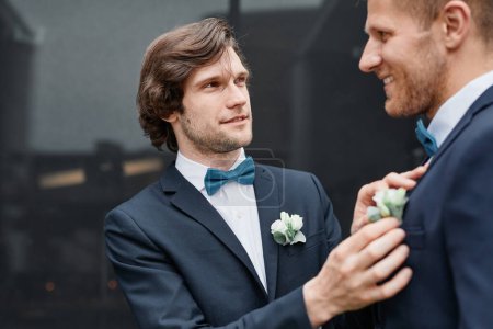 Photo for Portrait of smiling young man fixing grooms boutonniere during wedding ceremony, same sex marriage concept - Royalty Free Image