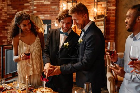 Photo for Portrait of young gay couple cutting cake together during wedding reception, same sex marriage - Royalty Free Image