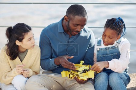 Photo for Portrait of male teacher showing robot model to two children outdoors during engineering class - Royalty Free Image
