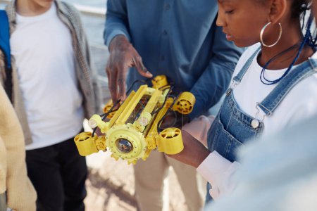 Photo for Close up of young black girl holding robot model during engineering class outdoors with teacher helping - Royalty Free Image