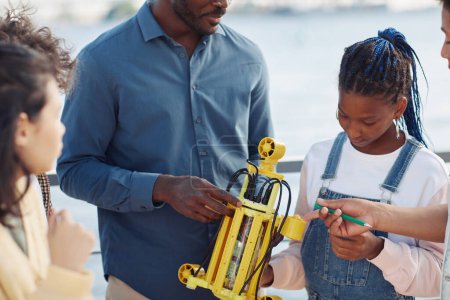 Téléchargez les photos : Plan recadré d'un enseignant noir démontrant un modèle de robot à un groupe d'enfants à l'extérieur - en image libre de droit
