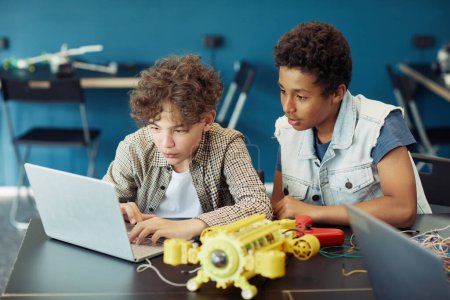 Téléchargez les photos : Portrait de deux adolescents utilisant un ordinateur portable et un robot de programmation pendant les cours d'ingénierie à l'école - en image libre de droit