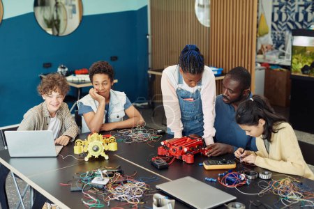 Téléchargez les photos : Groupe diversifié d'enfants avec professeur mâle construisant des robots ensemble pendant les cours d'ingénierie à l'école - en image libre de droit